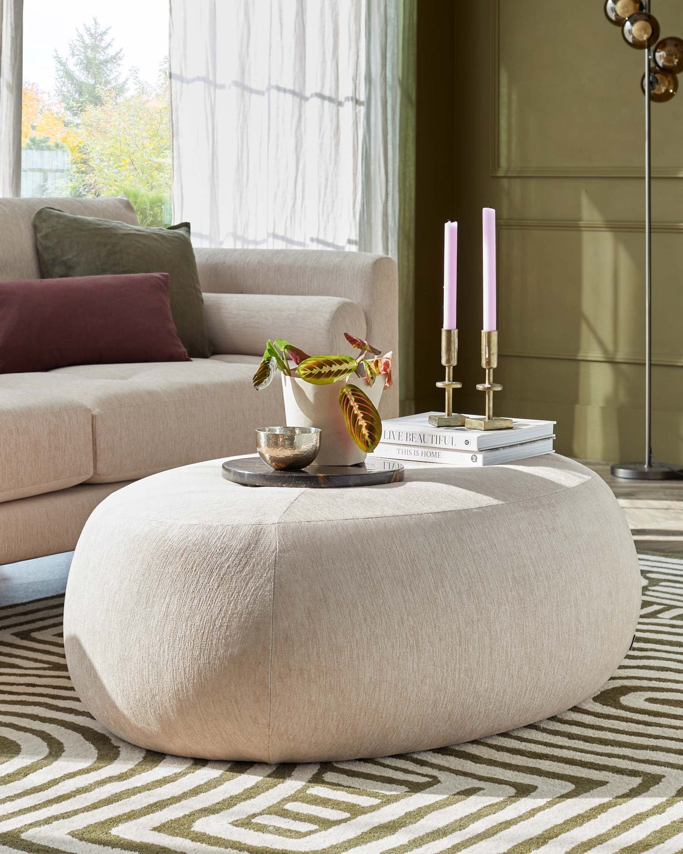 Round beige fabric ottoman in a contemporary living space, with a soft texture and a versatile design suitable for seating or as a coffee table alternative.