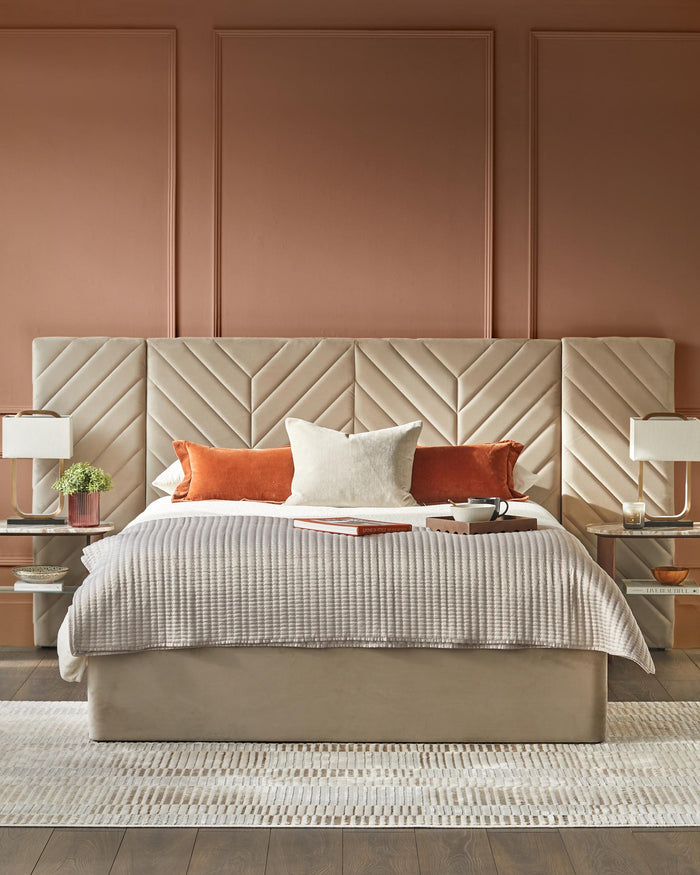 A stylish bedroom setup with a large, upholstered headboard, bedside tables, lamps and a comfortable bed with pillows and a quilt.