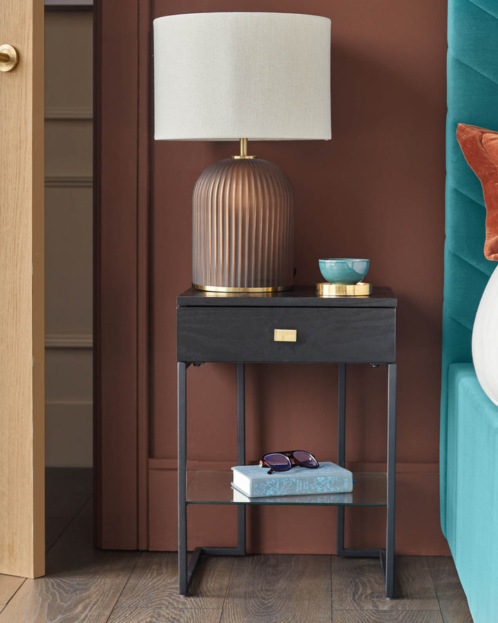A nightstand featuring a drawer, glass shelf, lamp, book and spectacles. Perfect for bedroom storage.