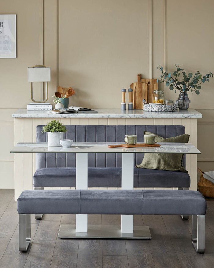A modern dining set with a glass table, upholstered banquette seating, and a sleek bench with metal legs.