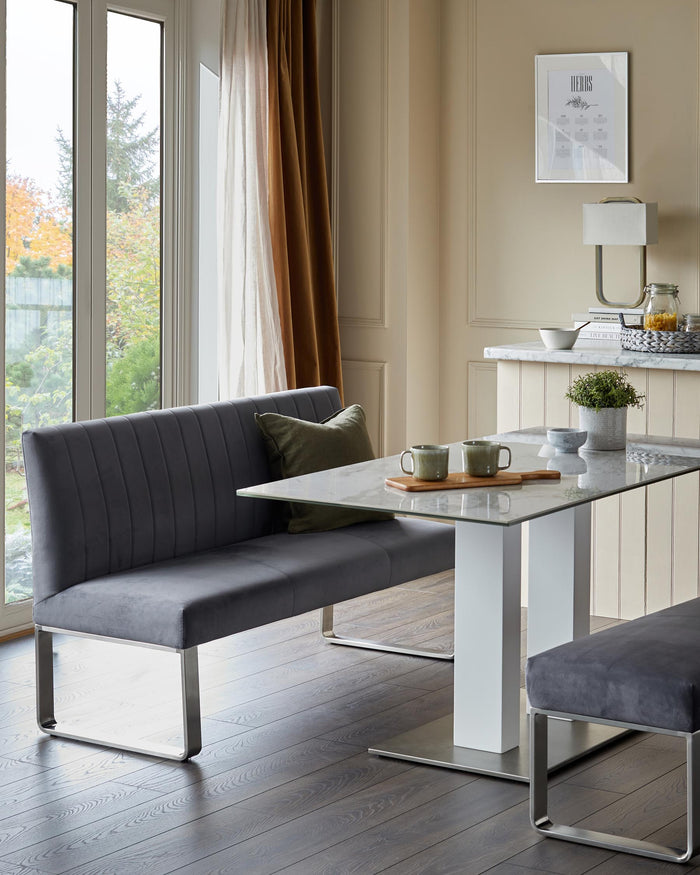 A dining set with grey upholstered bench seating, a marble-topped table and grey upholstered stool. Modern, stylish design.