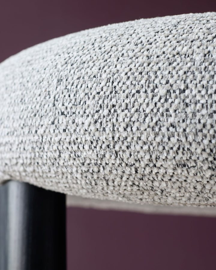 Close-up of textured grey fabric seat with a black leg against a dark plum wall. A stylish addition to any home.