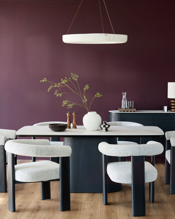 A modern dining set featuring upholstered chairs, a marble-look table, and a sideboard, all under a circular pendant light.