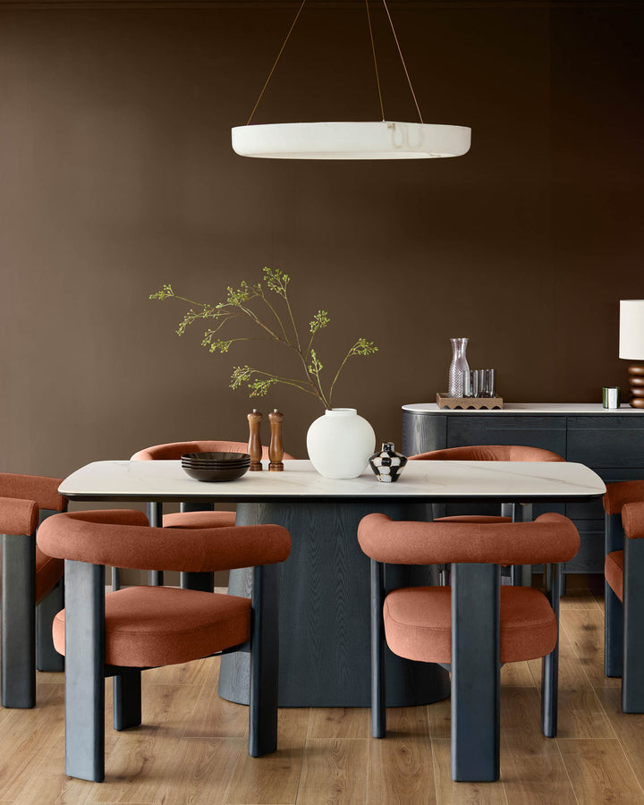 Toffee-red fabric dining chair with curved backrest and cylindrical legs, shown at dining table.