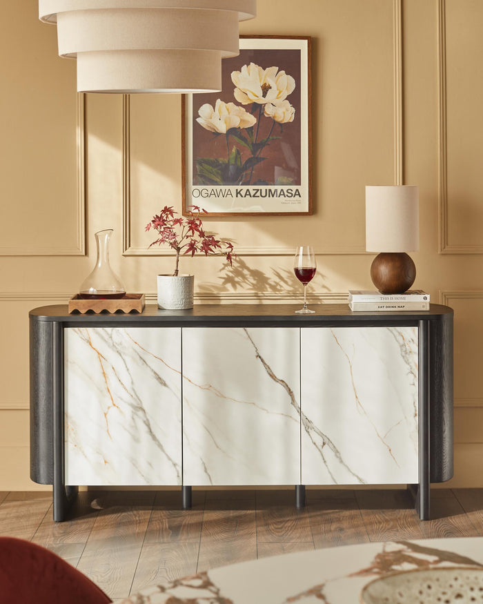 A stylish sideboard with marble-effect doors, topped with decorative items and a lamp.