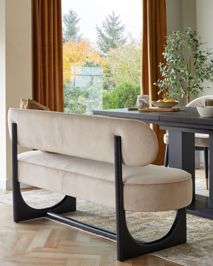 A modern dining bench with a curved backrest and sleek, black frame sits alongside a dark wood dining table.