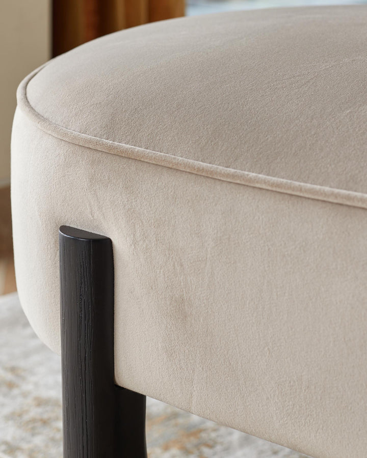 Close-up of a stylish, upholstered stool with a dark wooden leg. Soft, neutral colour palette.