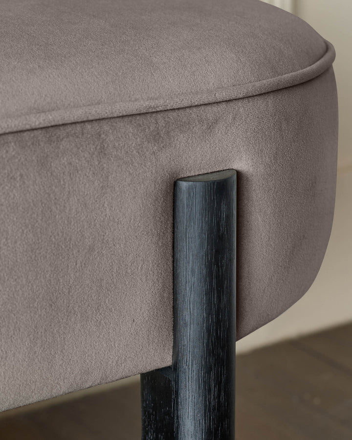 Close up of a stool with taupe velvet cushioning and a dark wooden leg. The fabric is soft and the leg is sleek and modern.