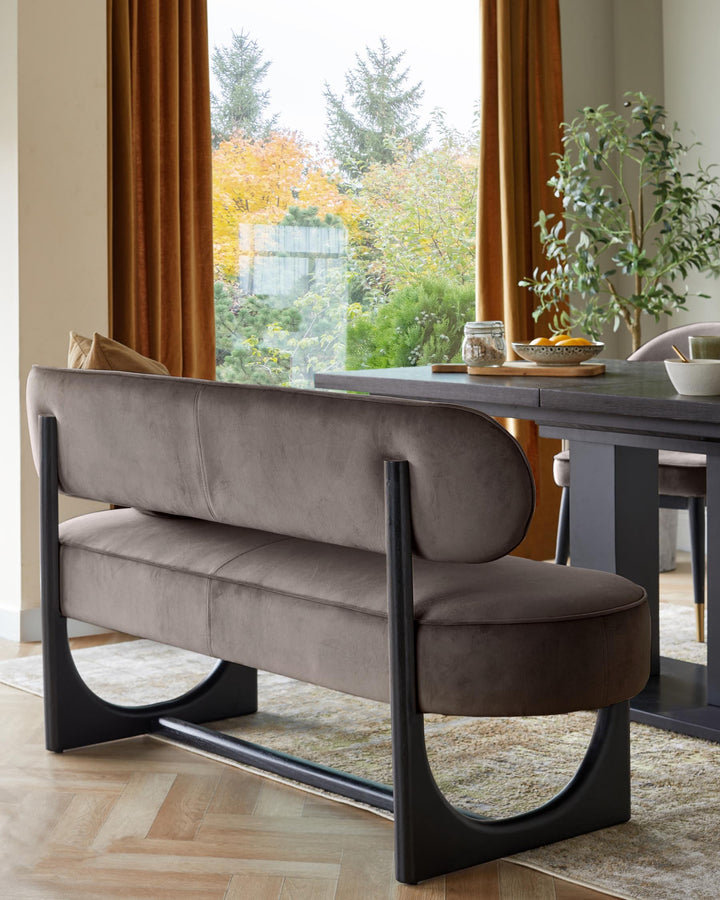 A contemporary dining set with a stylish velvet bench, dark wood table, and a view of autumn trees through the window.