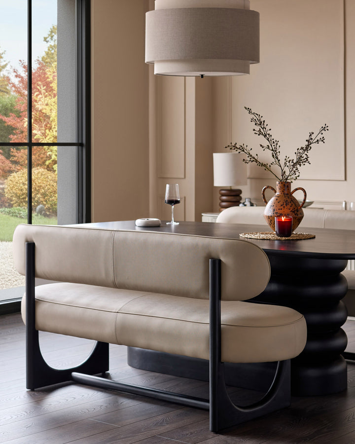 Orlan 3-seating dining bench with backrest in natural faux leather, black frame, curved design in modern room setting.