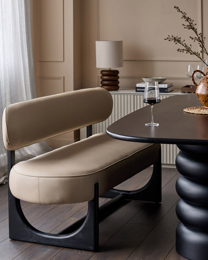 Orlan 3-seating dining bench with backrest in natural faux leather, black wood base, curved design, styled in modern interior.