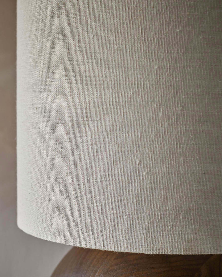 Close-up of a lamp with a textured, neutral shade and a wooden base, displaying the intricate details of the materials.