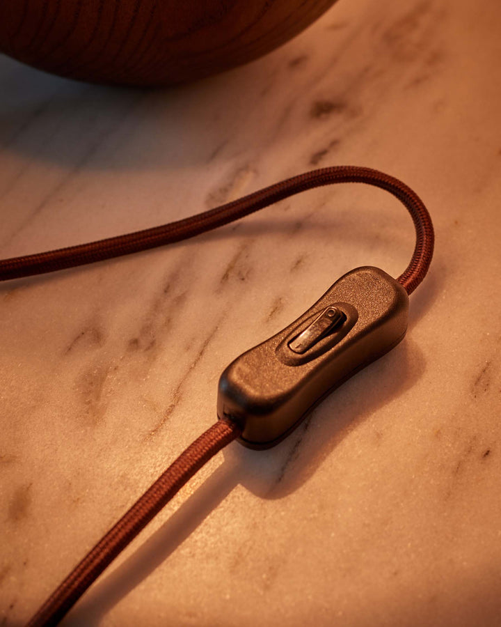 A close-up of a lamp cable switch on a marble surface, with a wooden object partially visible in the background.