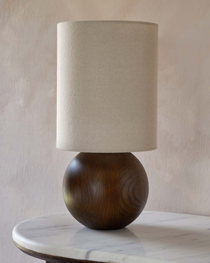 Stylish lamp with a wooden spherical base and a neutral-toned fabric shade, sat upon a marble table.