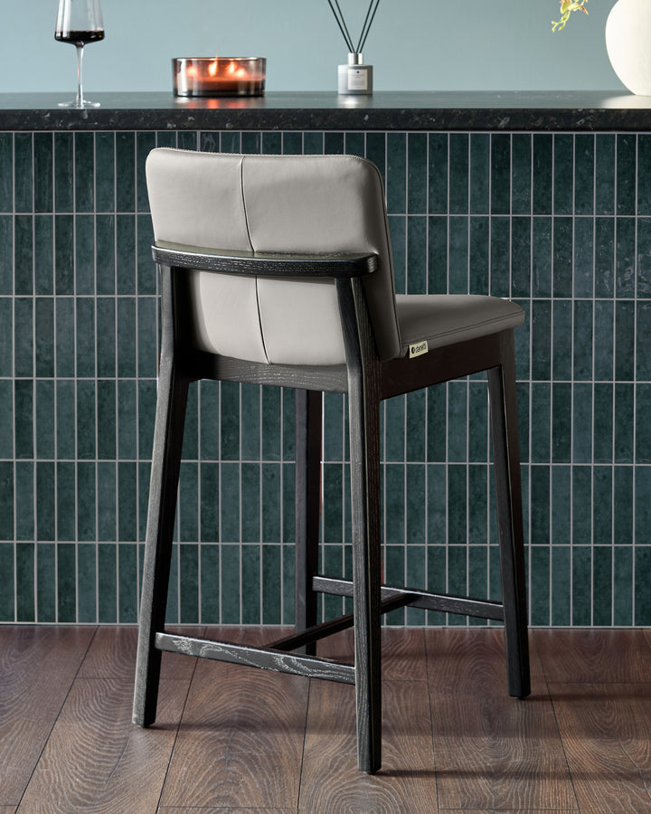 Otis bar stool in dark grey wood with cream leather seat and backrest, shown from rear angle at counter height.