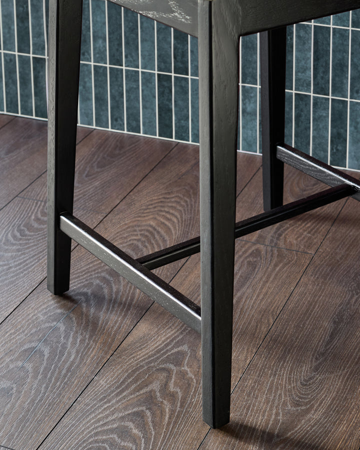 Dark grey leather bar stool with black metal frame and footrest, shown from side angle on wooden floor.