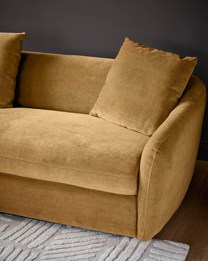 Ochre fabric left-hand corner chaise sofa with rolled arms and scatter cushions, angled view against dark background.