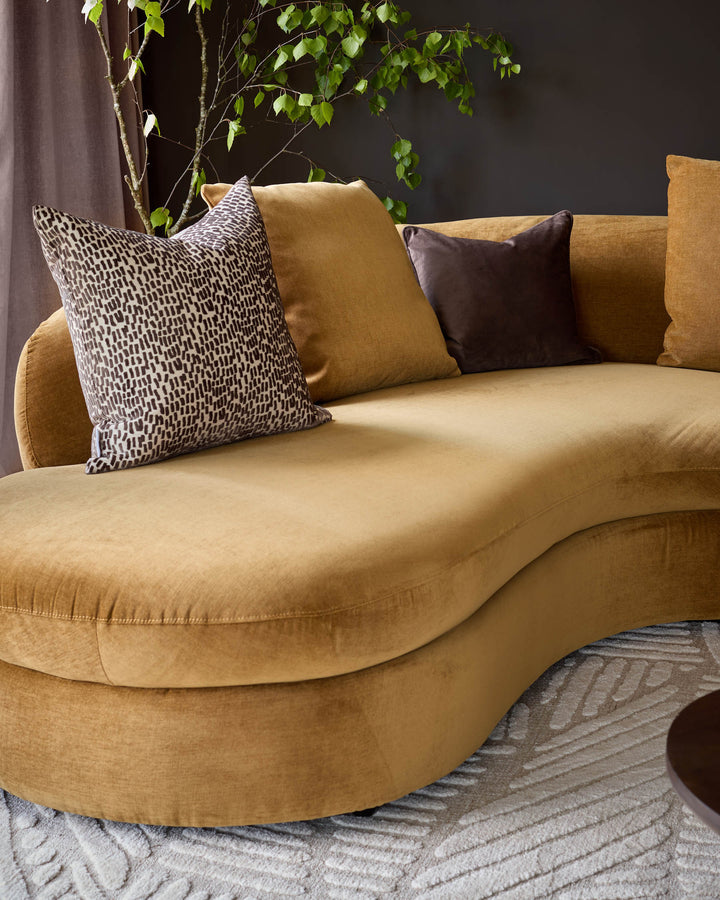 Ochre left-hand corner chaise sofa with curved design, styled with patterned and solid pillows, against dark wall with climbing ivy.