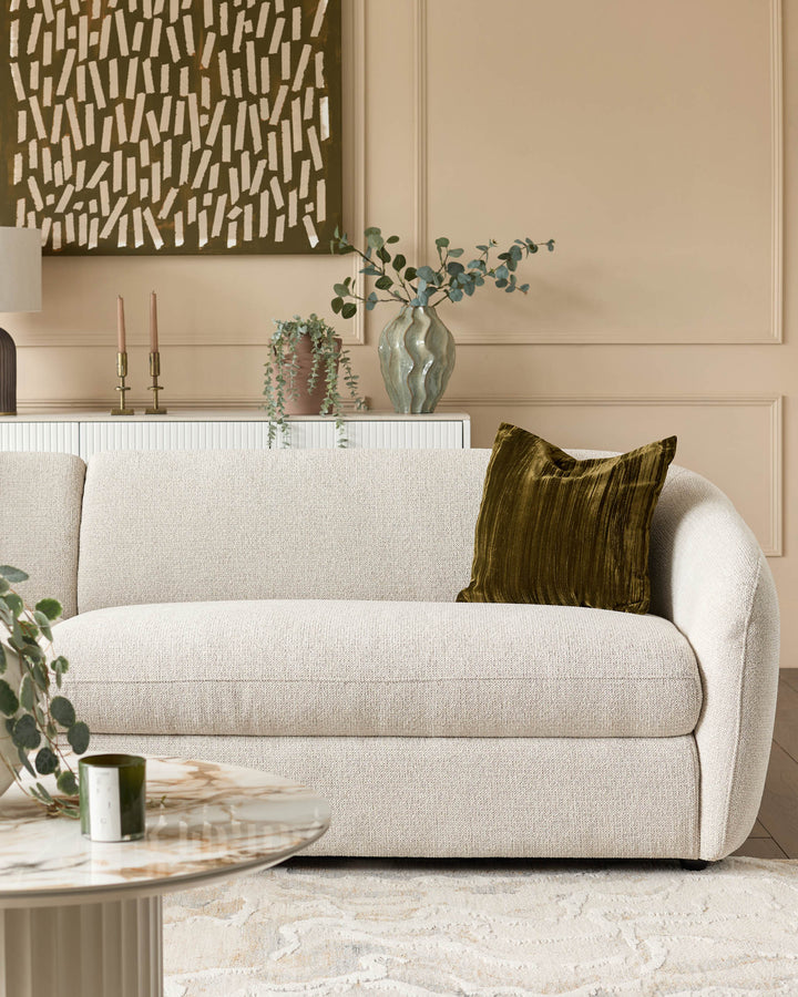 Cream fabric curved sofa with rounded arms, styled with olive pillow and displayed in a modern living room setting.