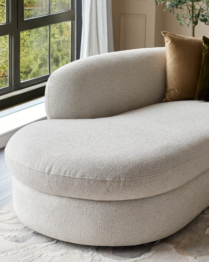 Cream fabric left-hand corner chaise sofa with curved design, positioned by a window with gold pillow accent.