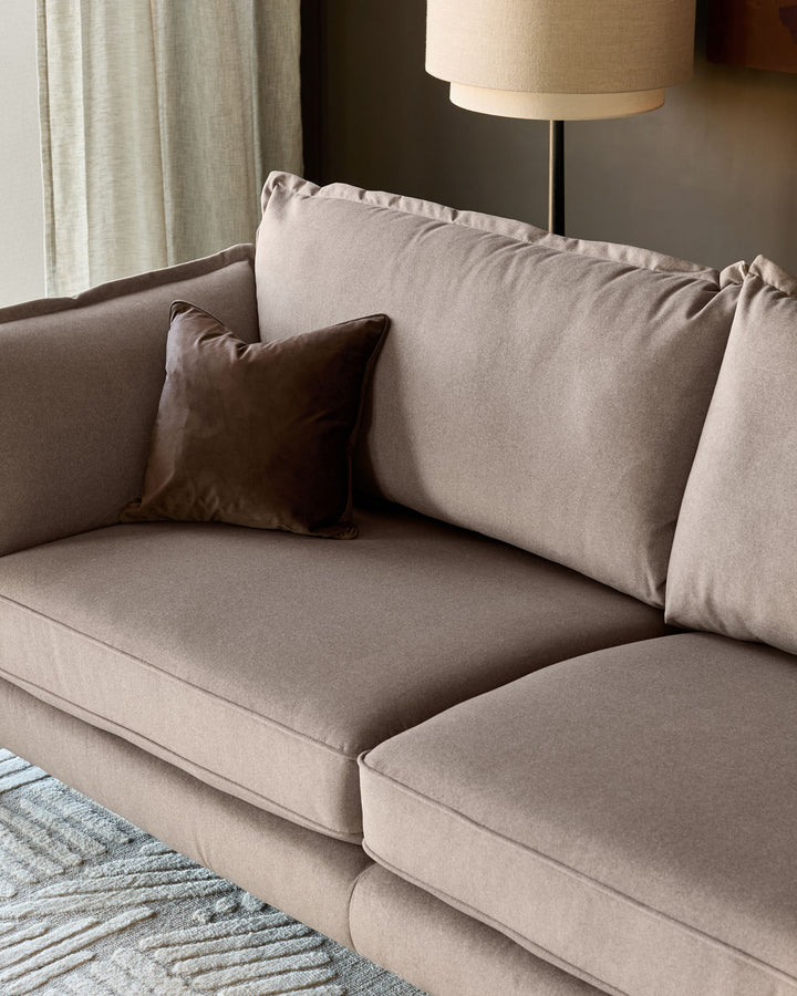 Otto 3-seater sofa in mocha fabric, angled view showing cushions and brown accent pillow in modern living room setting.