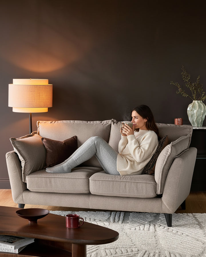 Otto 2-seater sofa in mocha fabric, displayed in a living room setting with a woman seated on it holding a mug.
