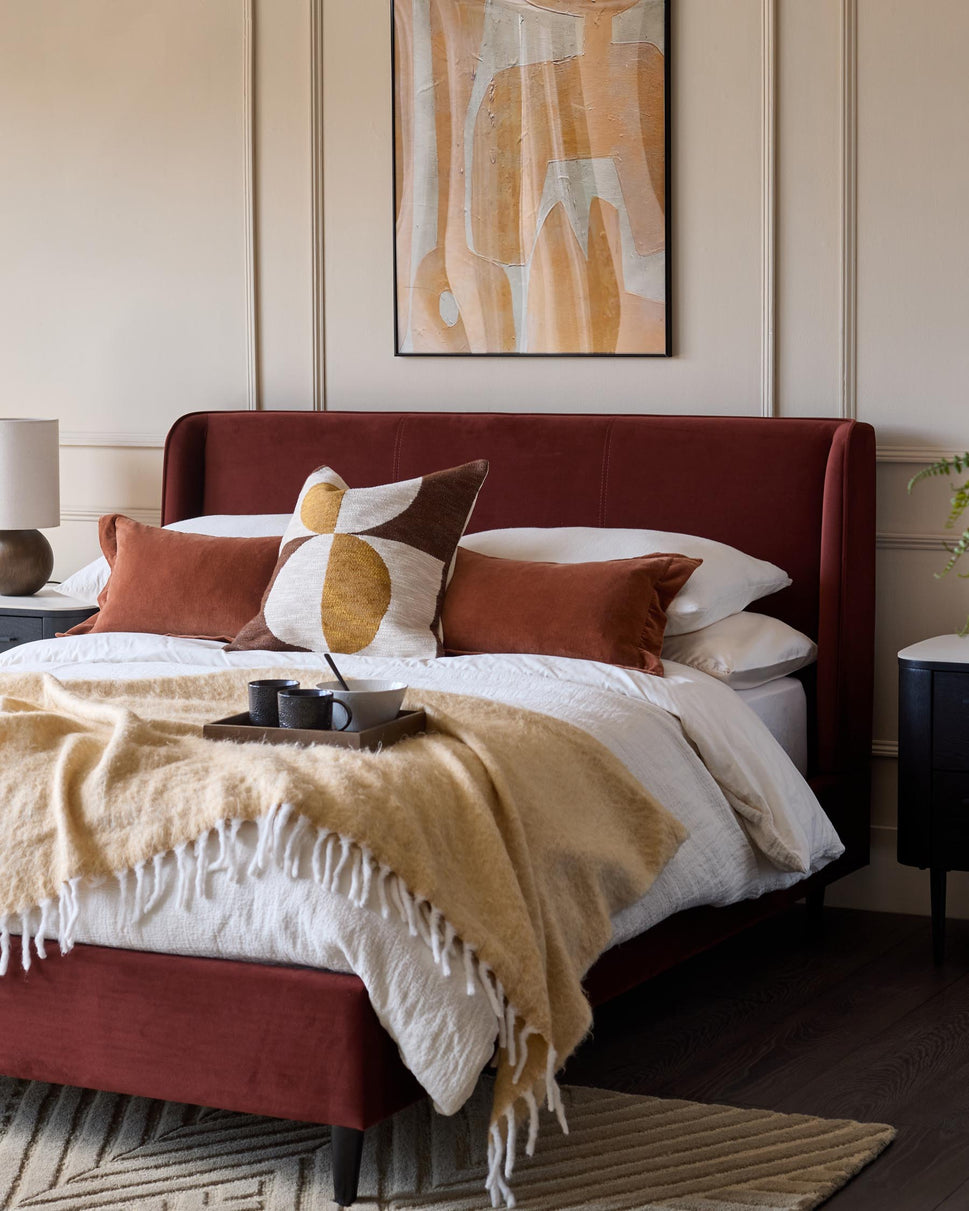 Bedroom features a red velvet bed frame, abstract artwork, and bedside tables. A cosy, modern design.