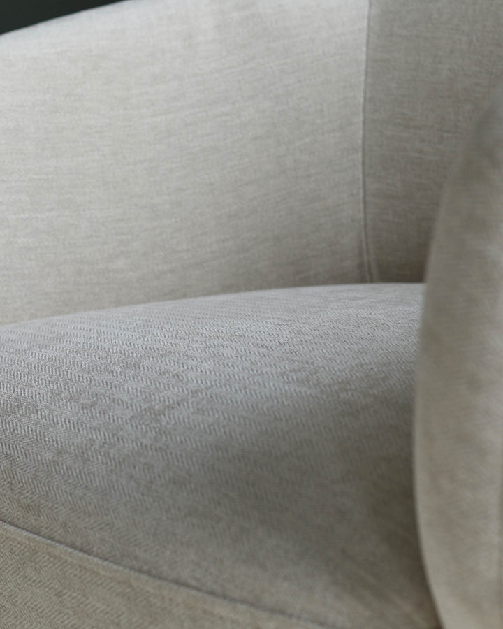 Close up of a cream coloured armchair with a textured fabric finish, showing seat and arm.
