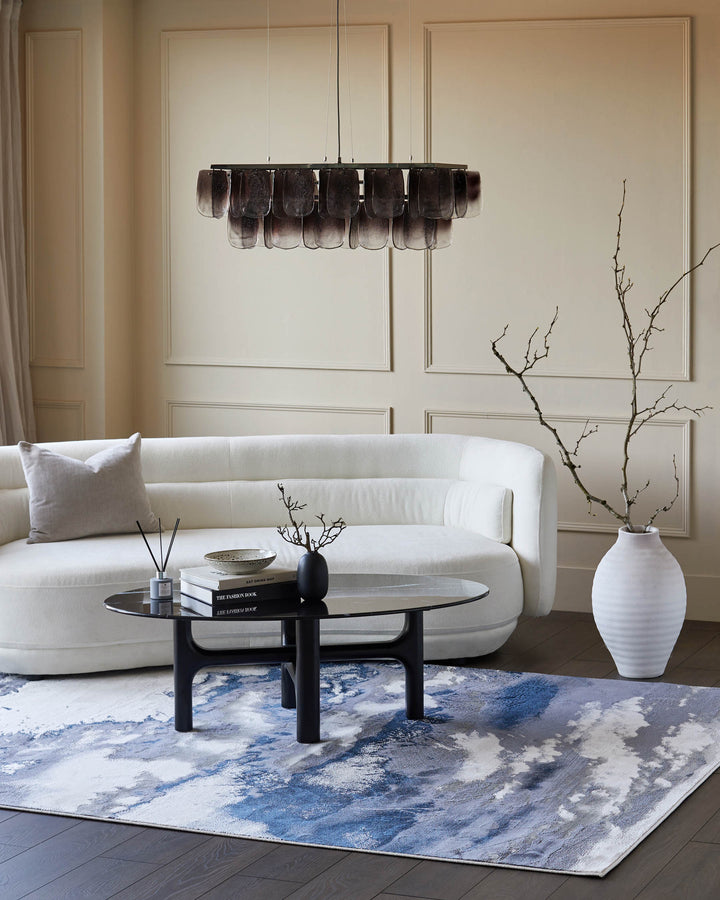 A stylish living room featuring a white sofa, black coffee table, patterned rug and lighting fixture.