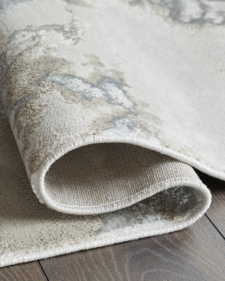 A rolled-up neutral coloured rug with a subtle pattern sits on top of a wooden floor.