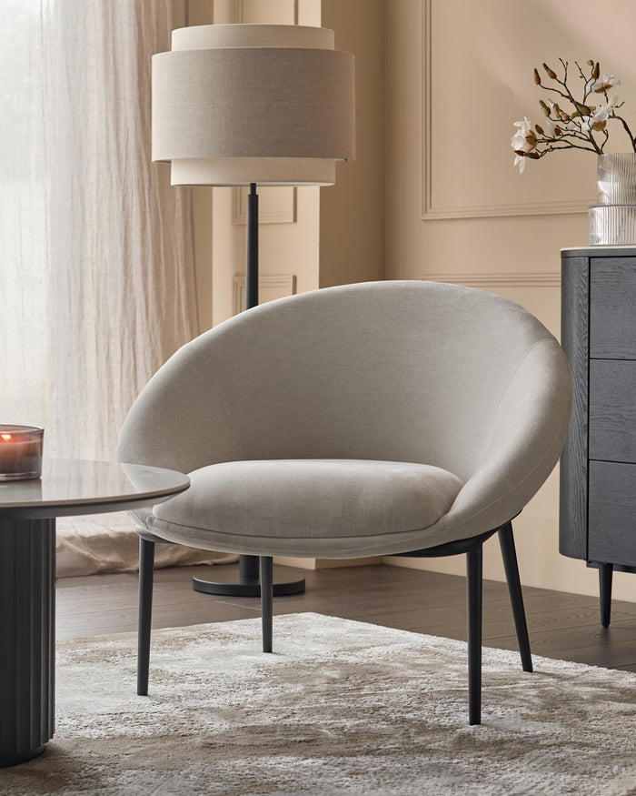 A stylish grey armchair sits beside a dark grey side table and cabinet, with a floor lamp providing gentle illumination.