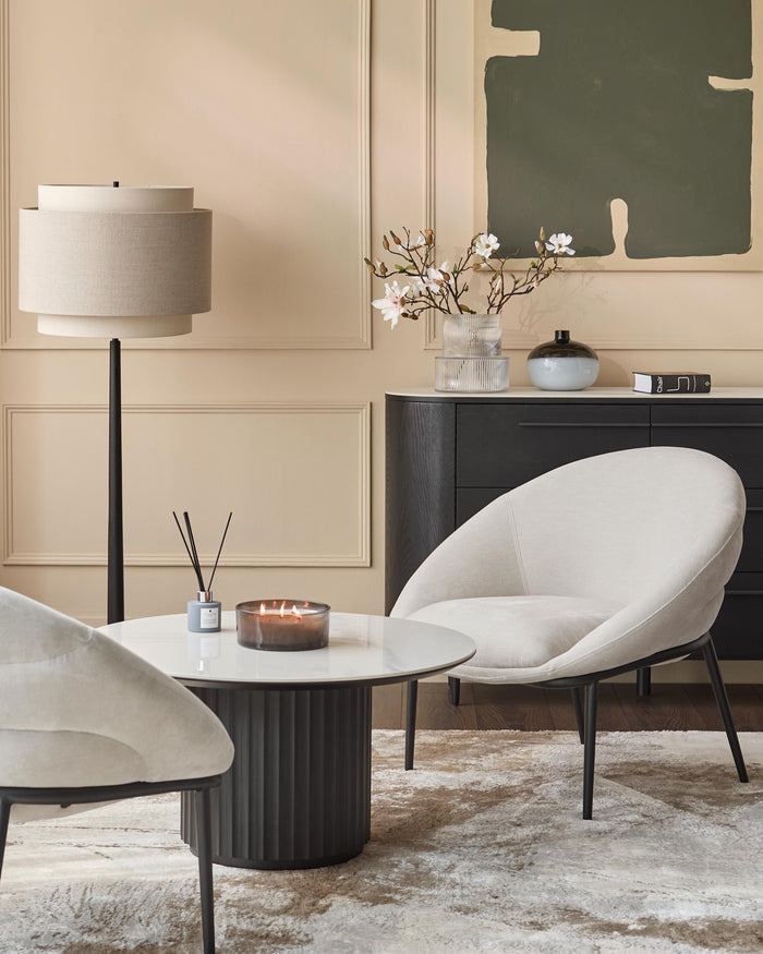 Modern furniture arrangement with chairs, round table, lamp, and sideboard featuring decorative objects.