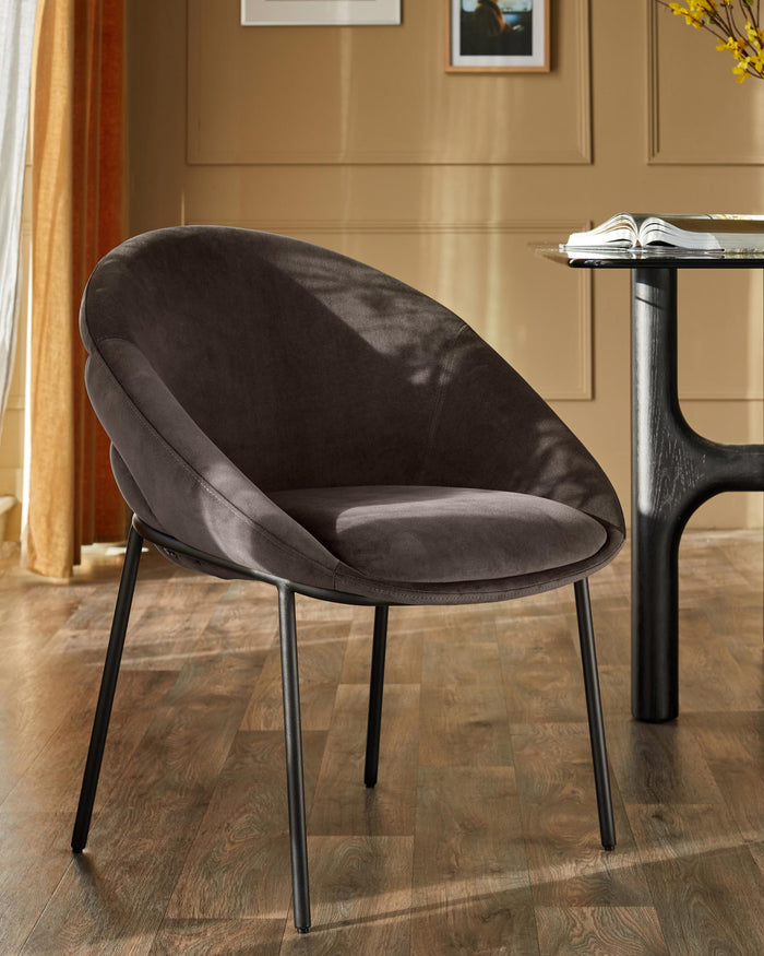 A stylish, brown, velvet chair with black metal legs sits beside a glass-topped table in a modern dining space.