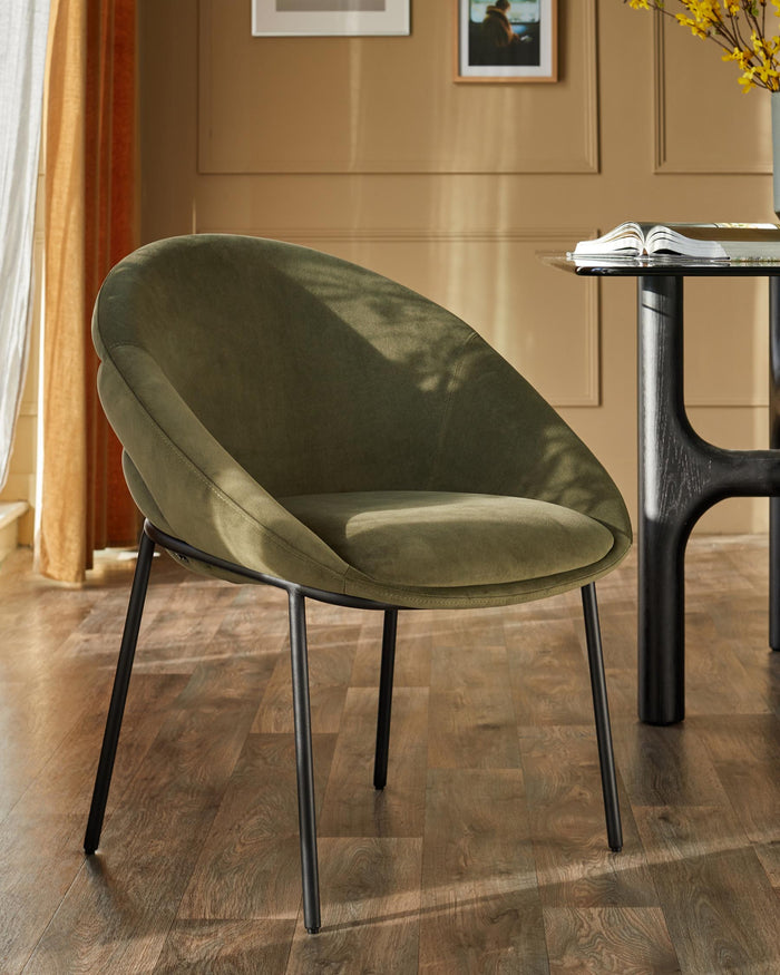 An olive green chair with black metal legs sits on a wooden floor next to a table.