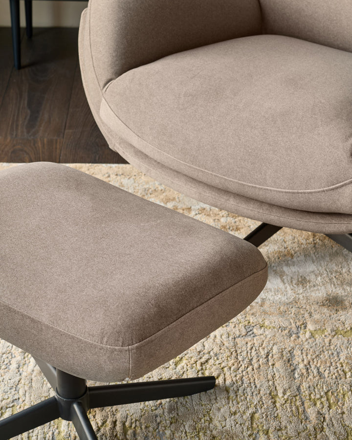 Mocha fabric accent chair and footstool with curved design on black legs, positioned on a cream textured rug.