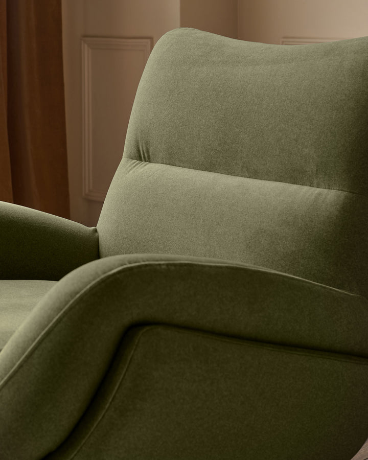 Piper accent chair with footstool in olive green velvet, shown at an angle highlighting curved backrest and armrest.