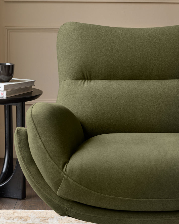 Piper accent chair with footstool in olive green velvet, curved design, shown in styled living room setting.
