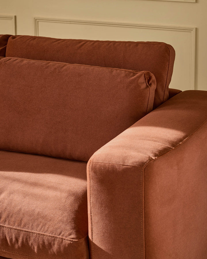Quinn 2-seater sofa in toffee red fabric, showing curved armrest and cushioned seat from side angle.