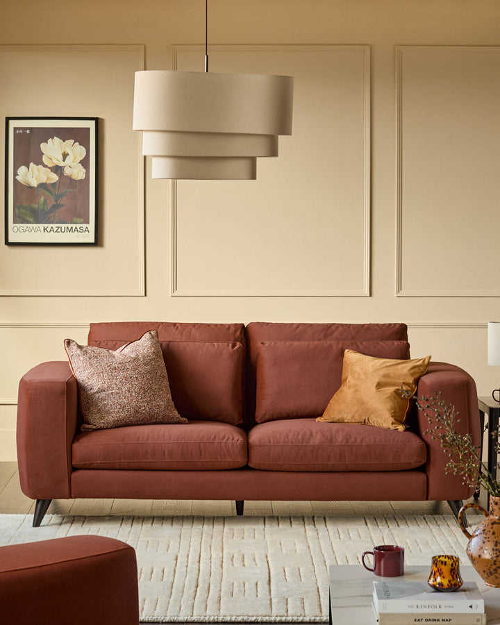 Burleigh 2-bulb pendant light in natural linen, displayed above a rust-colored sofa in a cream living room.