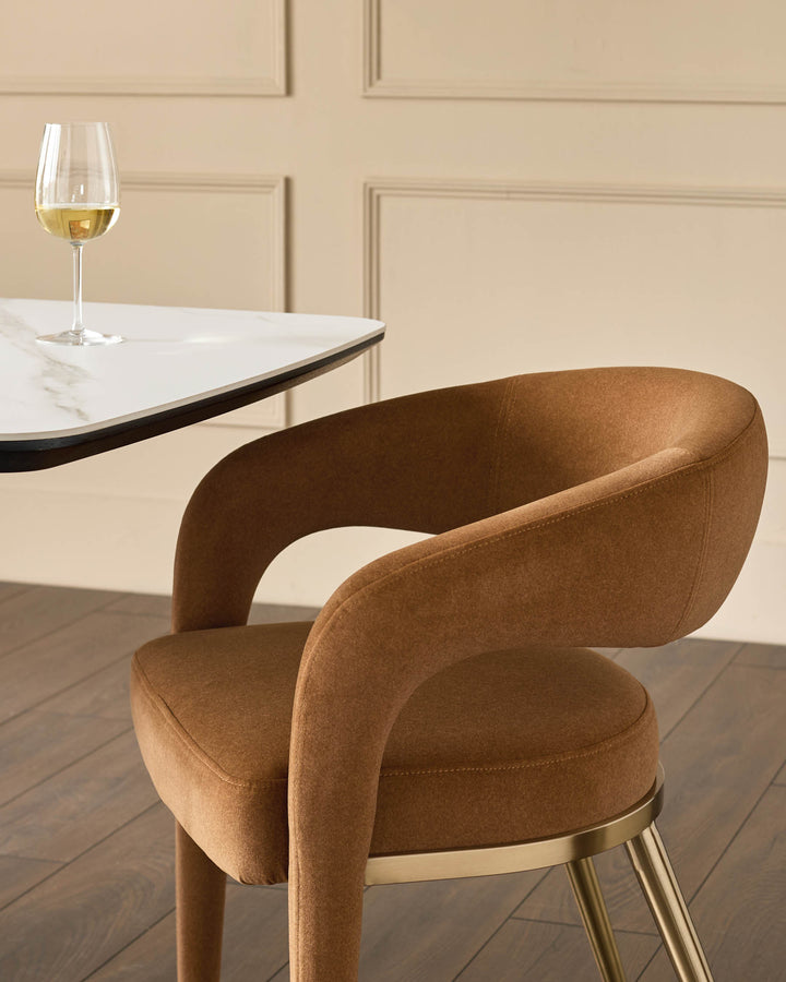 A stylish brown upholstered chair with a curved back, paired with a modern table and a wine glass.