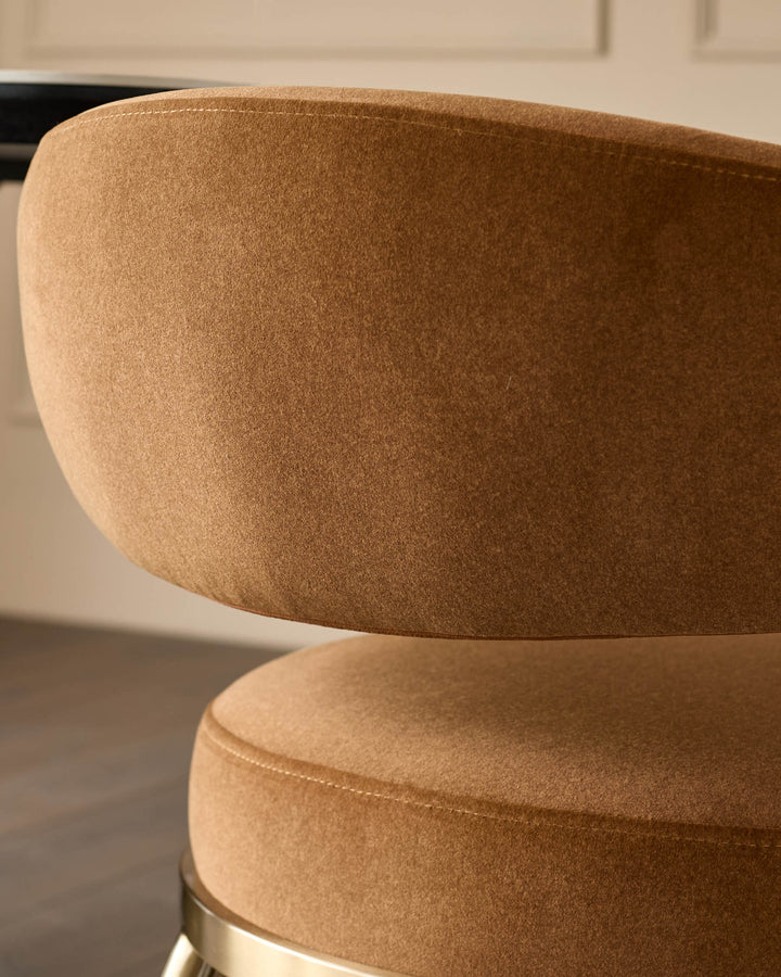 Close-up of a stylish brown upholstered chair with a curved back and a glimpse of a table in the background.