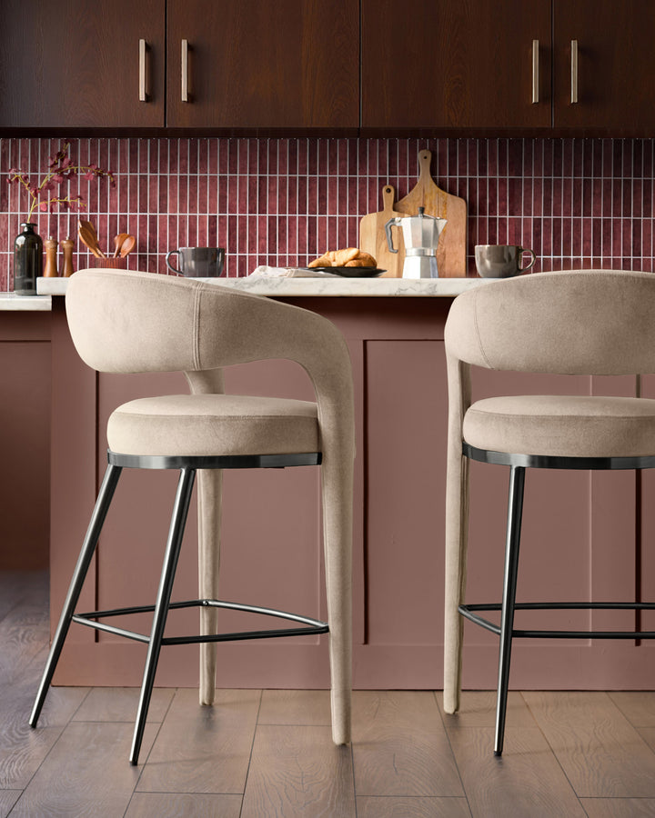 Champagne velvet bar stool with curved backrest, black metal legs, and footrest, shown at kitchen island.