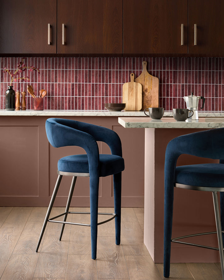 Rhett bar stool in dark navy velvet with curved backrest and metal legs, shown at kitchen counter.