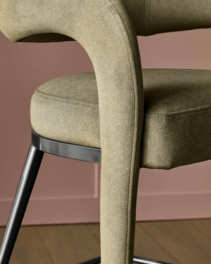 Rhett bar stool in olive-green fabric, close-up detail showing curved backrest and metal leg with accent band.