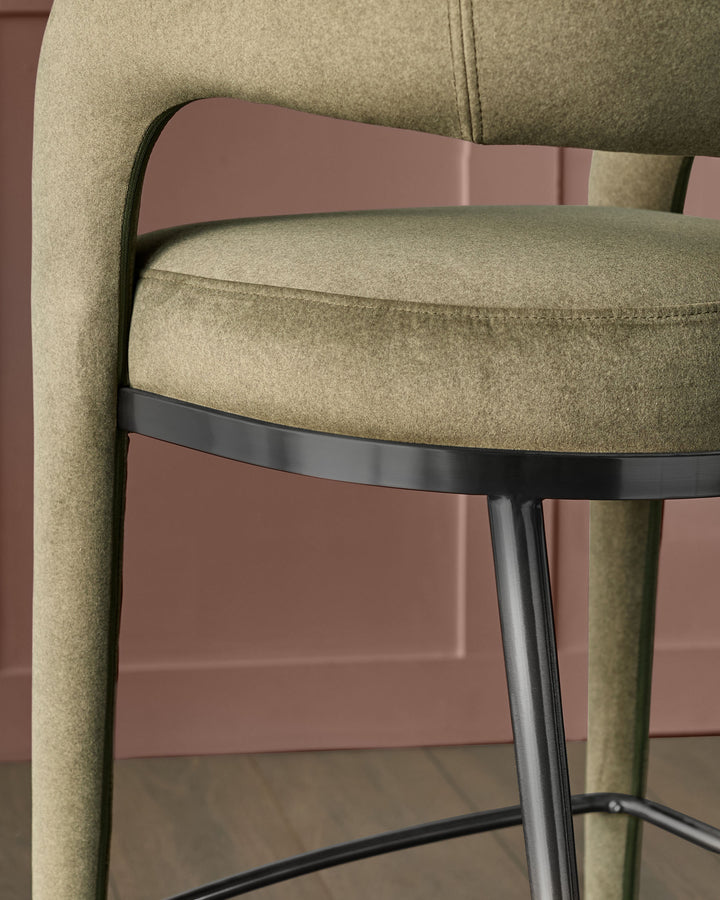 Rhett bar stool in olive green fabric with mauve metal frame, shown in close-up side view highlighting the curved backrest and seat detail.