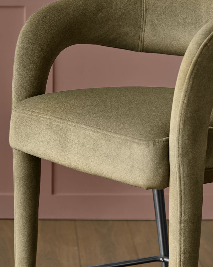 Rhett bar stool in olive green fabric with curved backrest and black metal legs, side angle view.