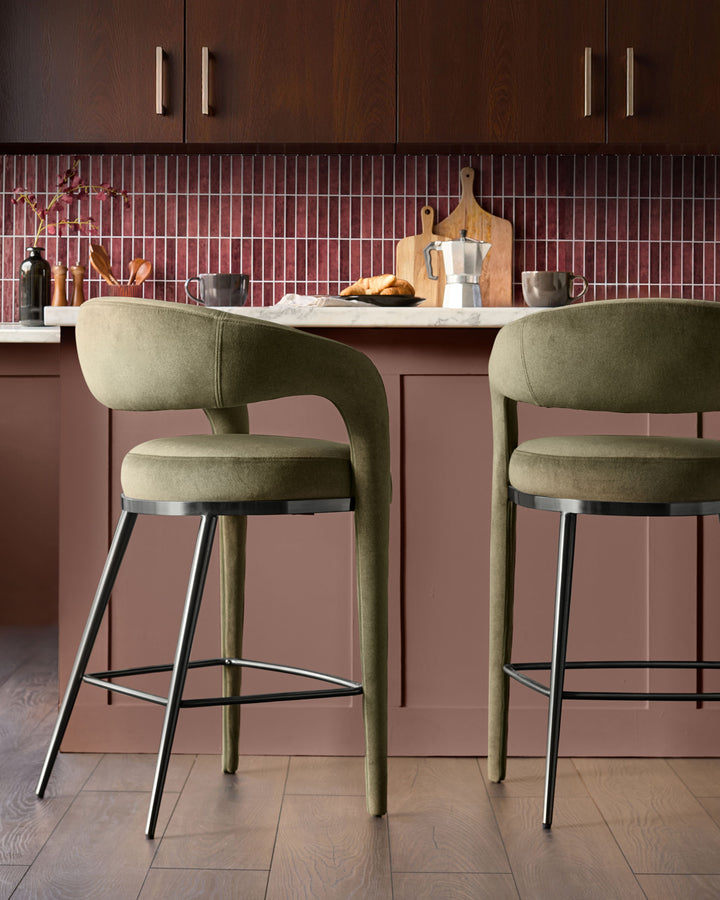 Olive green fabric bar stools with curved backrest and black metal legs at kitchen island with burgundy cabinetry.