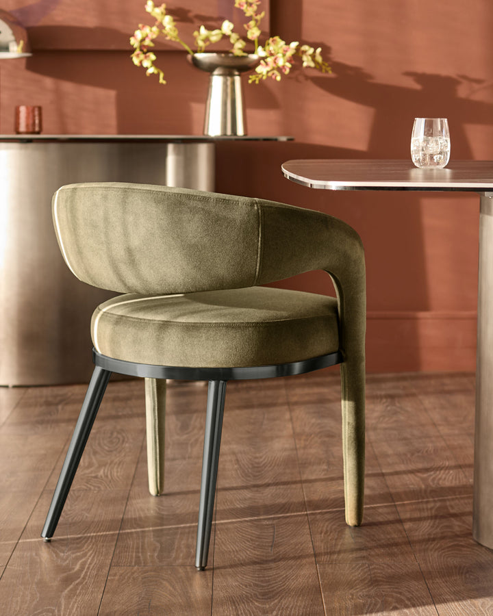 Rhett dining chair in olive green fabric with curved backrest, metal legs, shown in room setting at table.