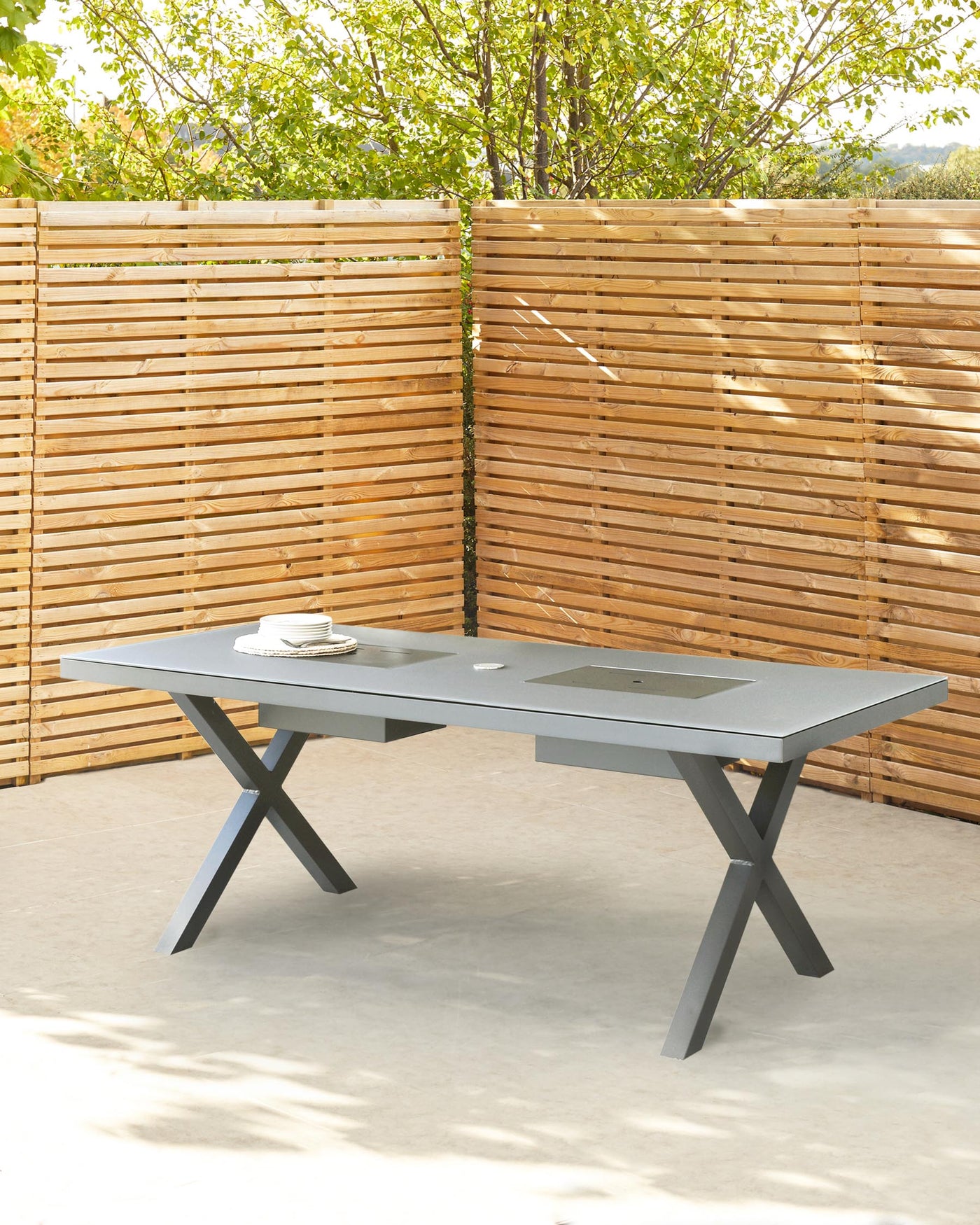 Modern outdoor dining table in a slate grey finish, featuring a spacious rectangular top with a central cut-out design, supported by distinctive crisscross legs.