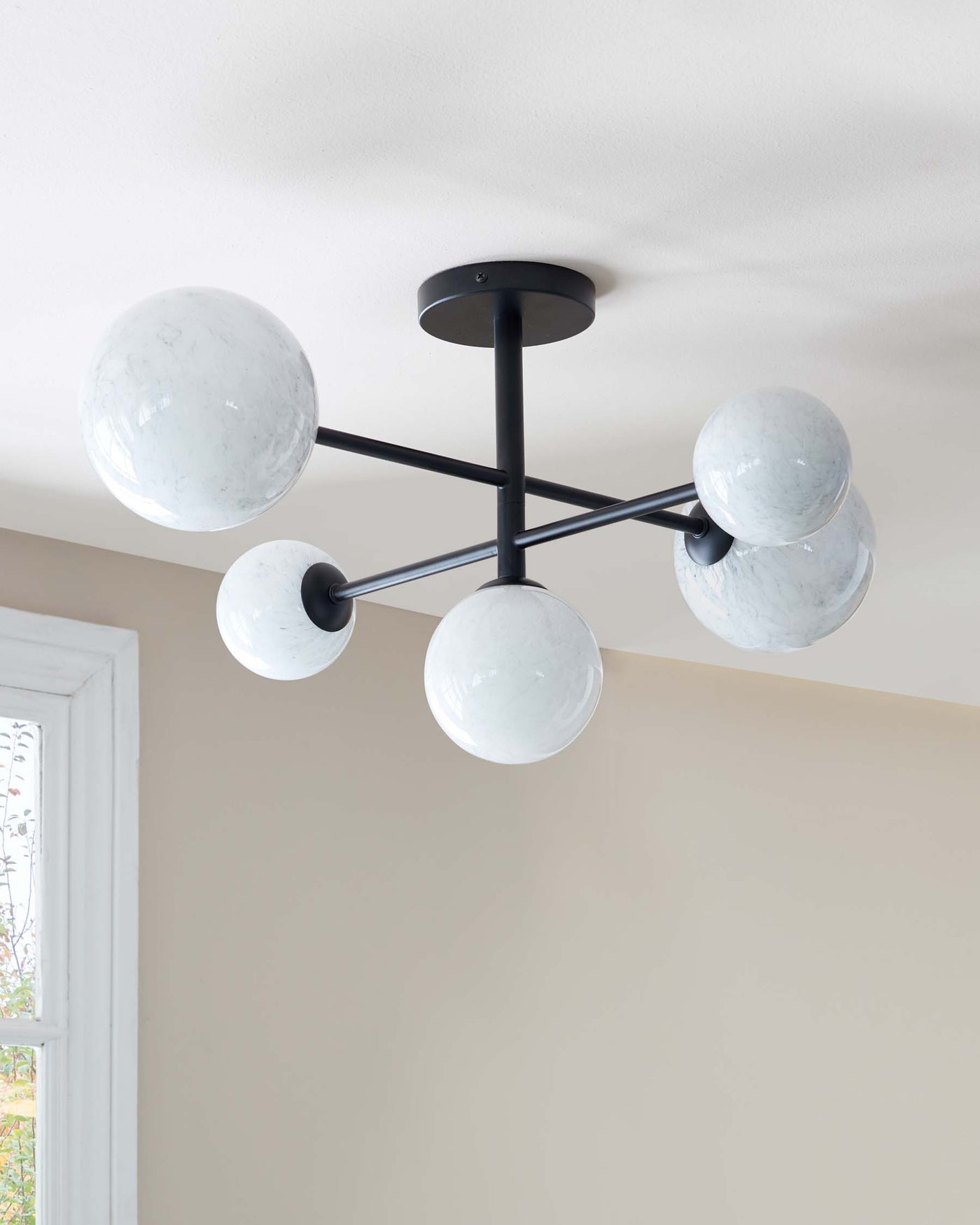 A modern-style chandelier with a matte black finish and five spherical, marbled glass shades affixed to linear arms, radiating from a central point in a semi-flush mount design.